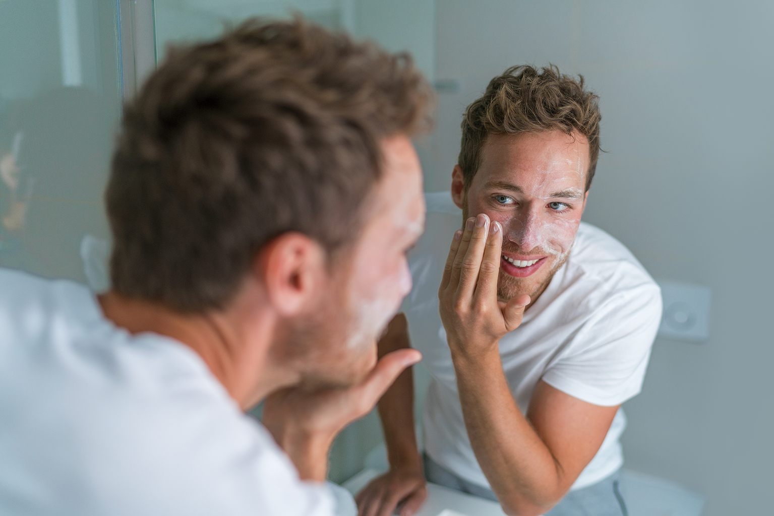man applying skincare product on face in bathroom