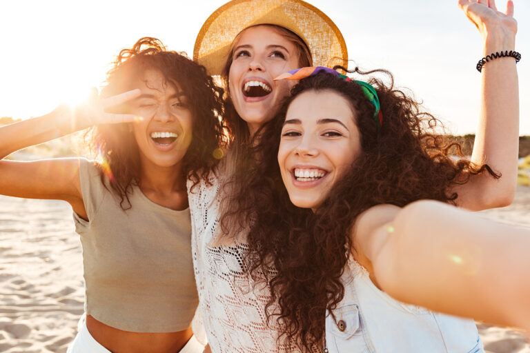 Three young women having fun on the beach smiling at camera.