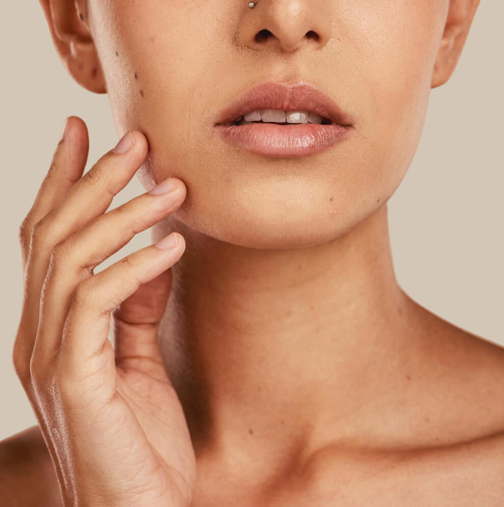 Close-up of a woman’s lower face and neck with a natural complexion, gently touching her cheek with her hand